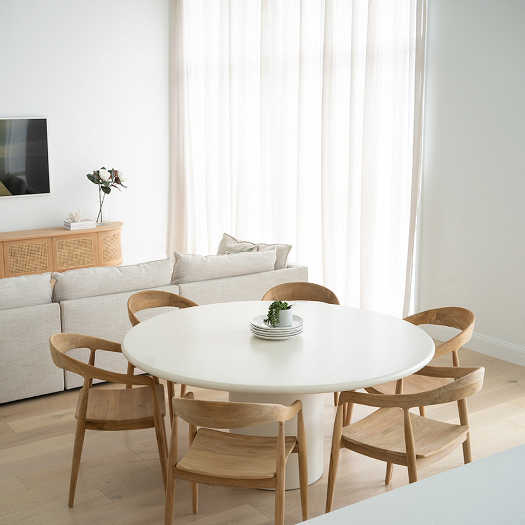 Angled lifestyle shot of Rigby Armchair – Natural with dining table in airy interior.