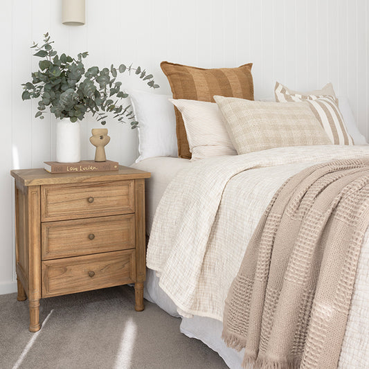Lifestyle side view of Hamilton 3 drawer bedside table – Natural styled with vase and greenery beside bed.
