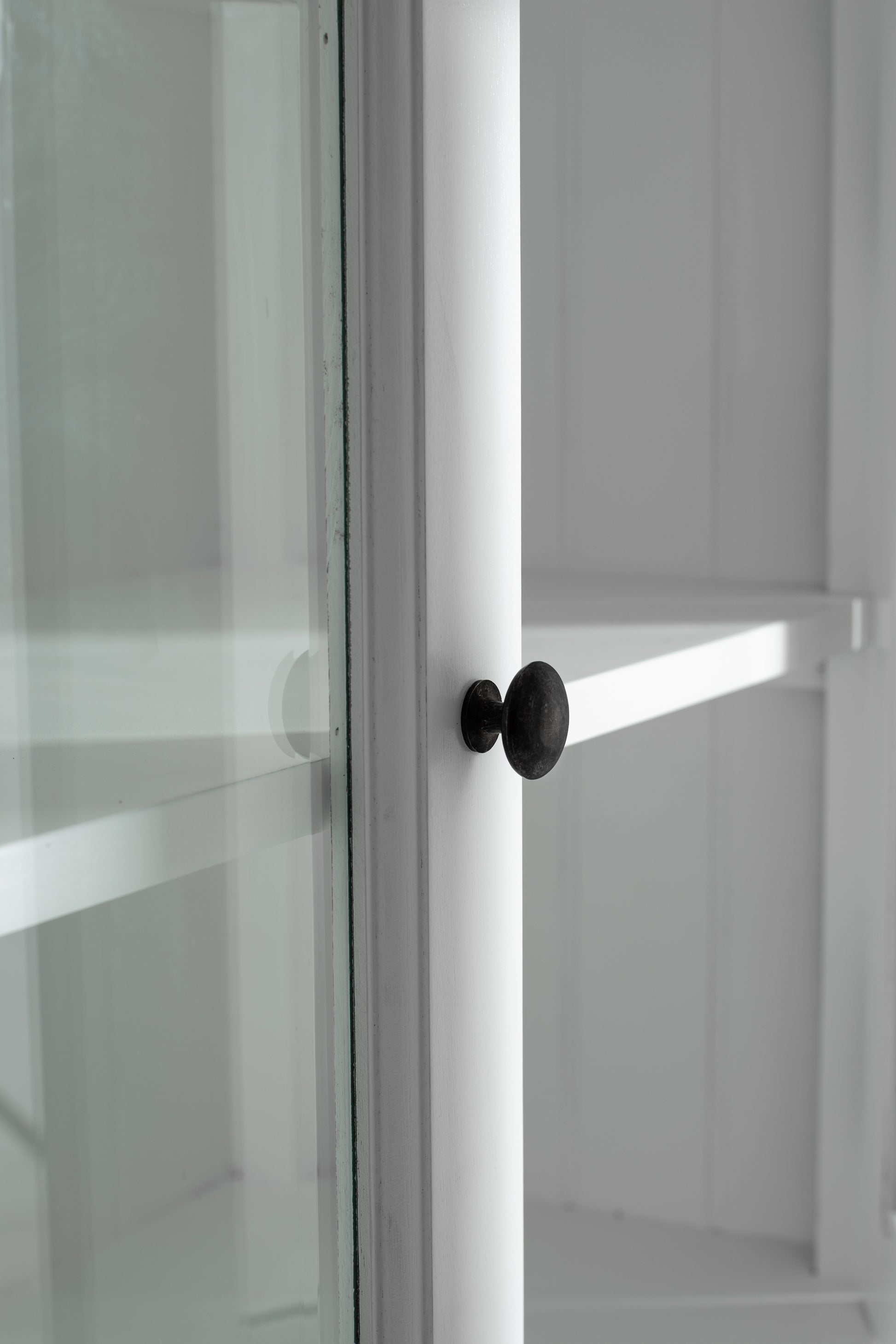 Close-up view of traditional 3 level white timber pantry black door knob and glass door.