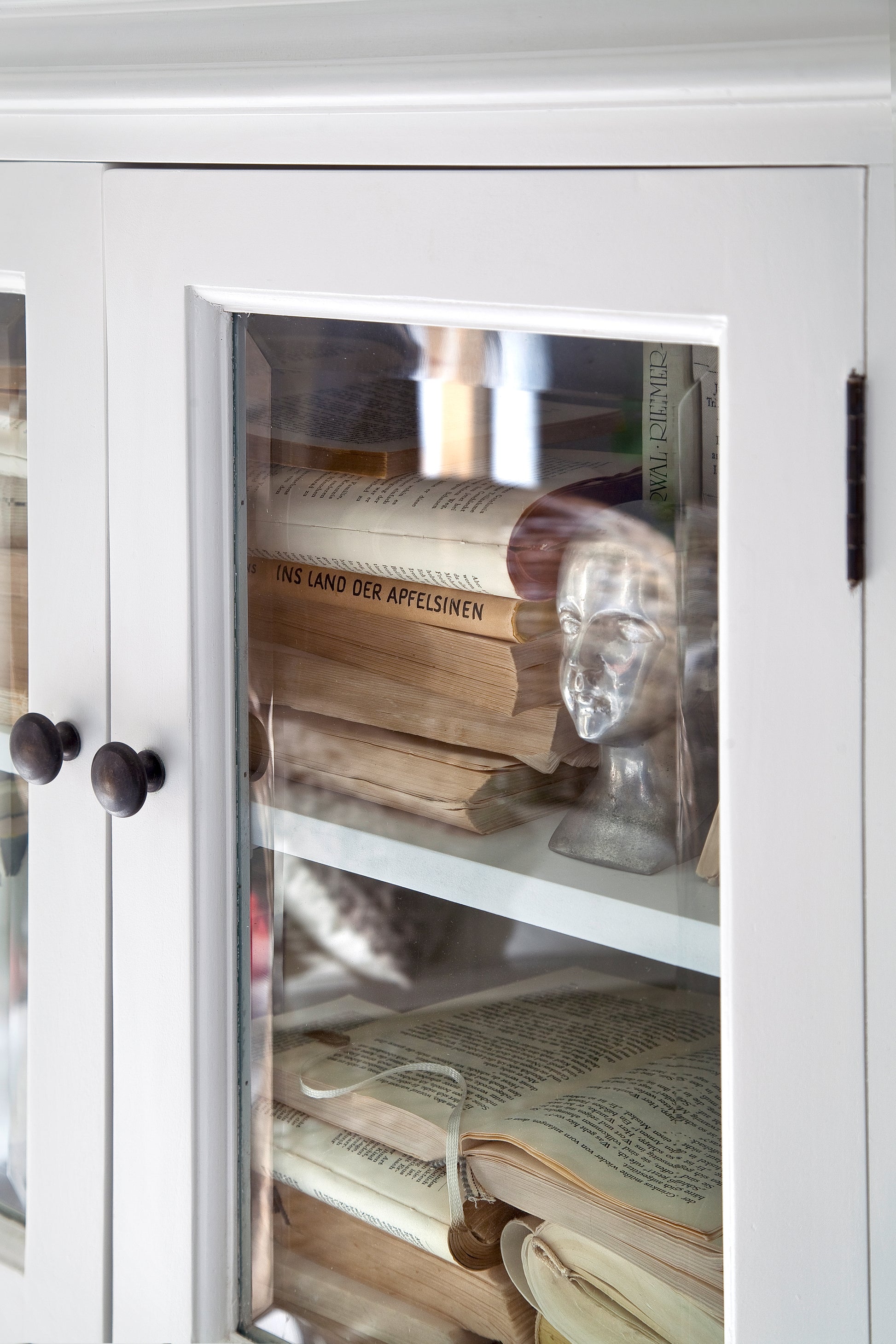 Close-up view looking through a glass door of a white timber cabinet at old books.