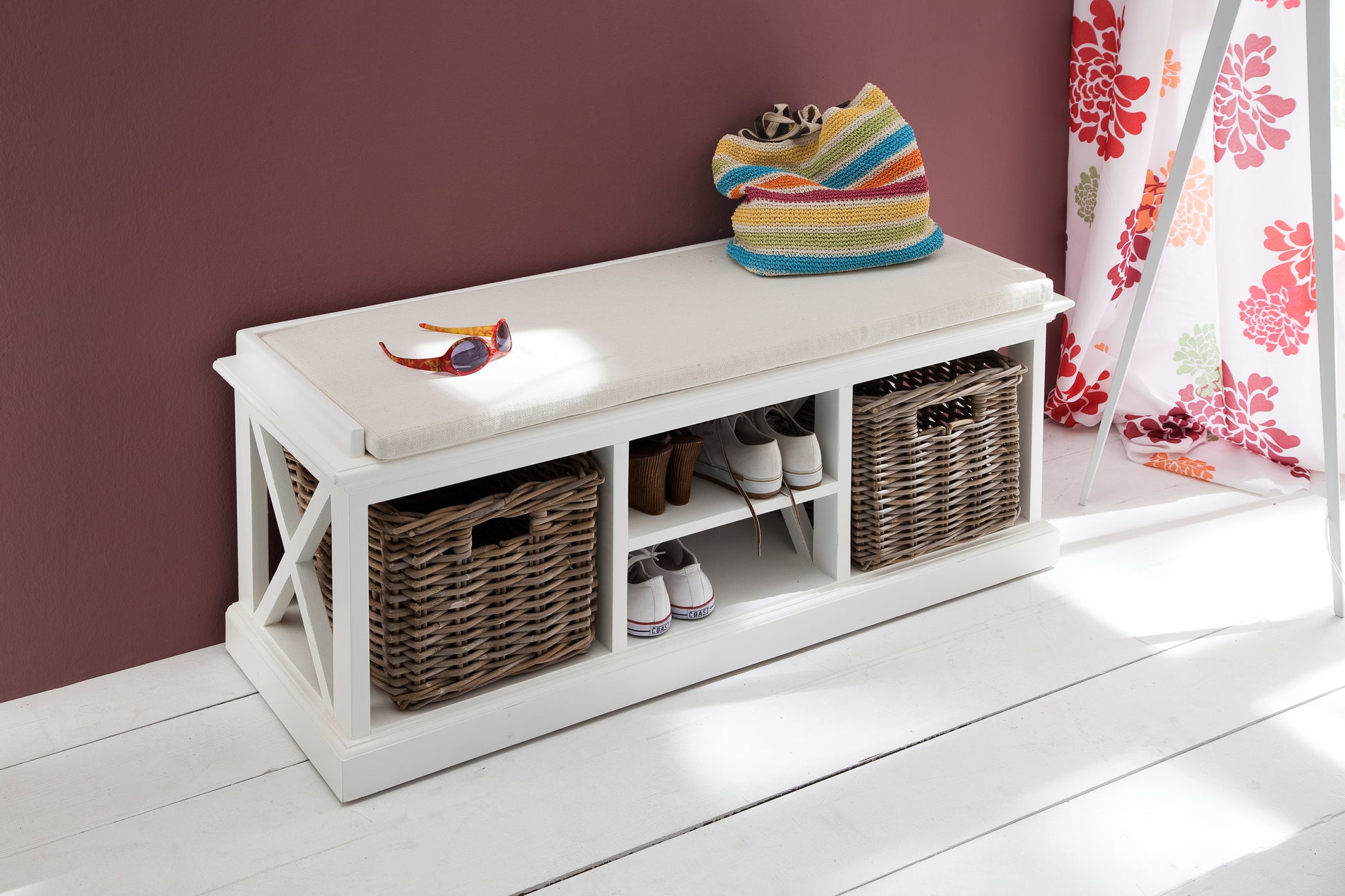 Slightly angled aerial view of a white timber bench with cushion and 2 basket set with shoes on shelves and sunglasses and towel on bench top.