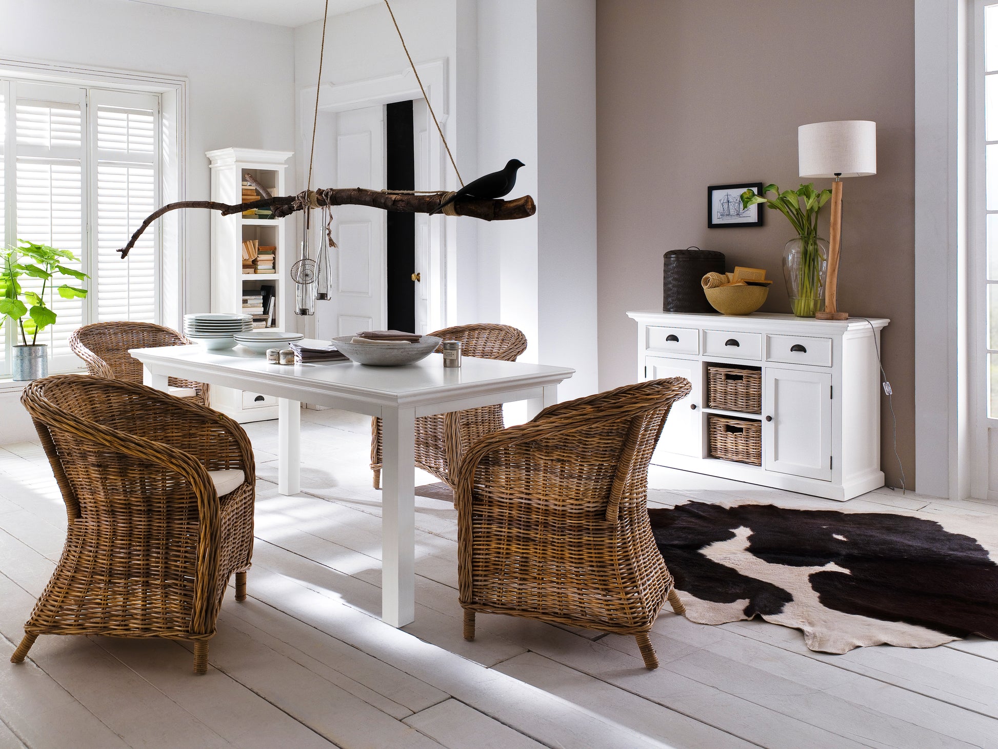 Dining setting featuring a white wooden dining table and 4 wicker armchairs accompanied by ta white wooden bookshelf and storage unit.