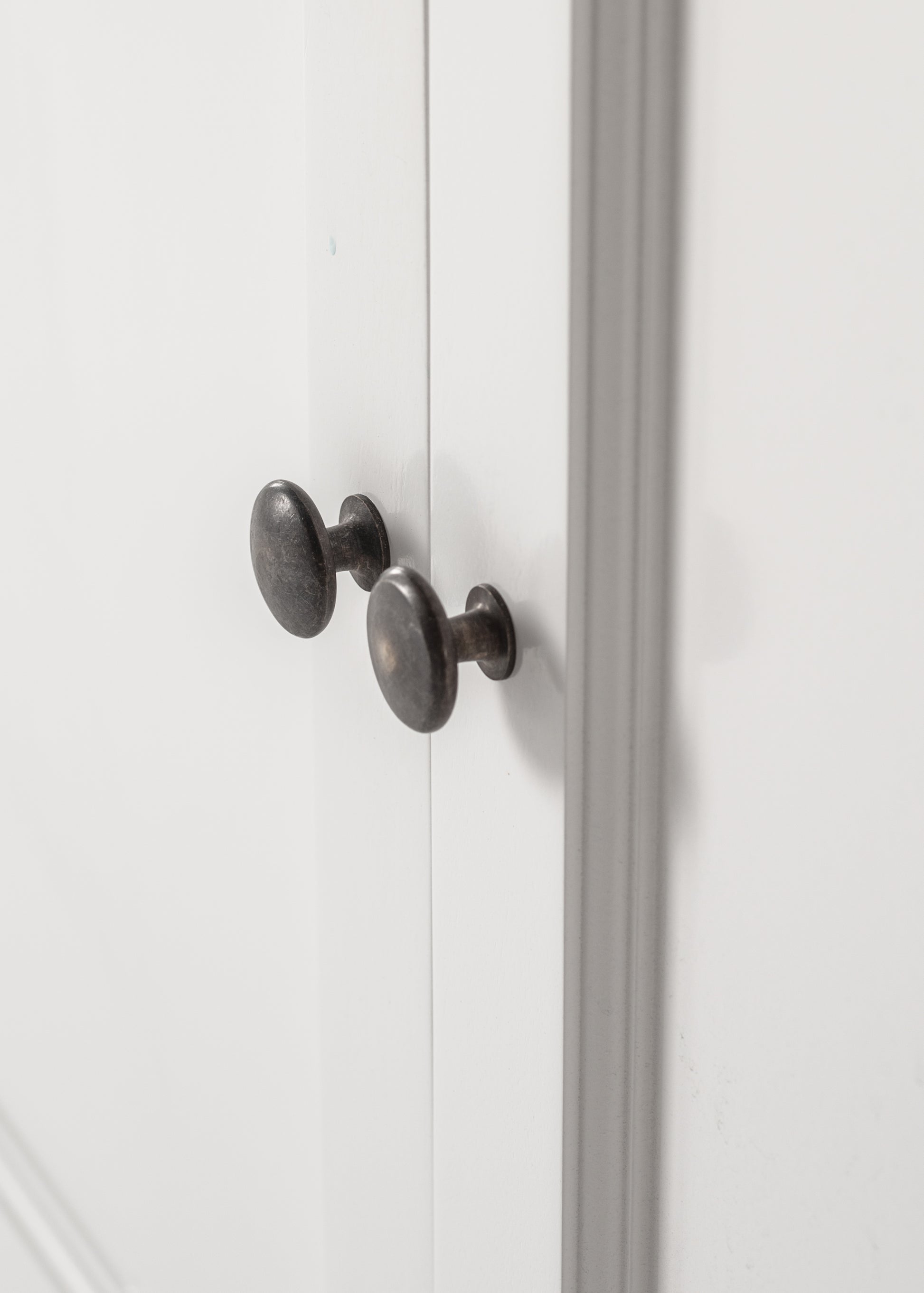 Close-up view of antique brass hardware on white wooden buffet doors.