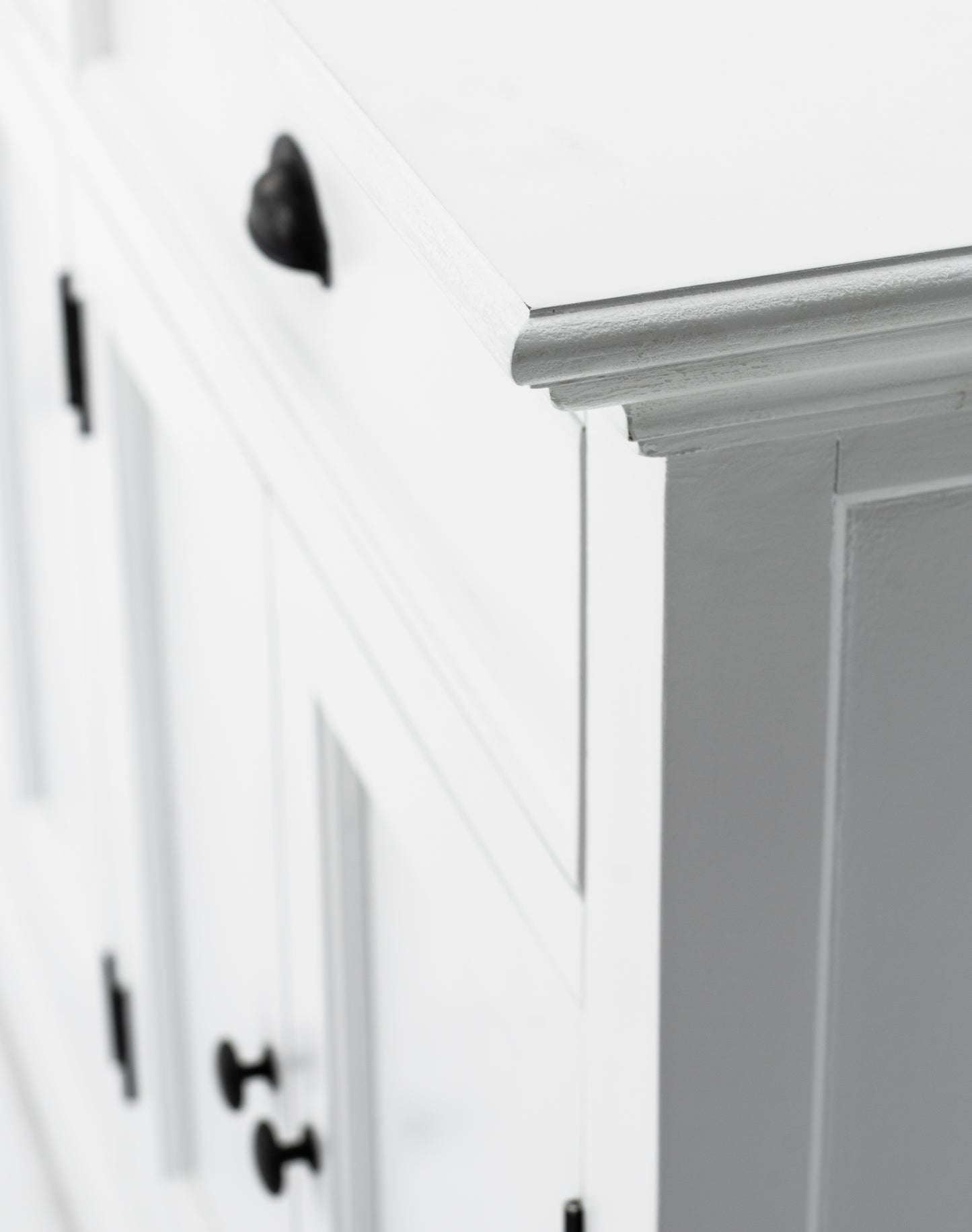 Close-up view of the corner of a white wooden buffet hutch base unit with antique brass hardware.