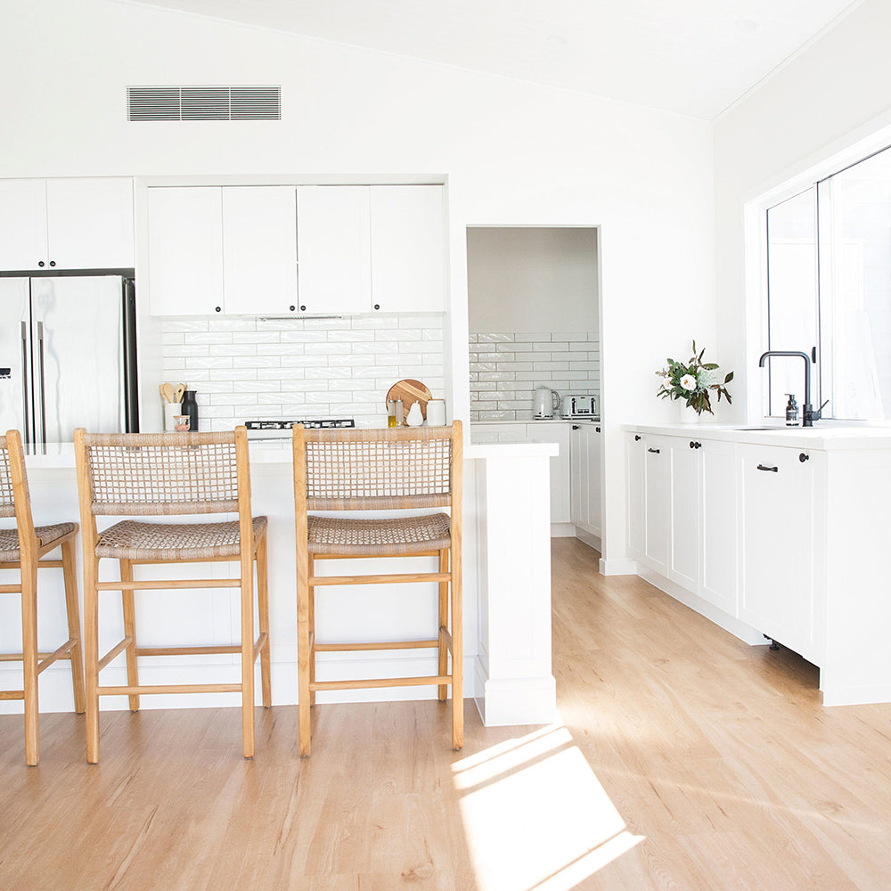 Interior kitchen setting featuring three Zen Bar Stools – Washed Grey – Open Weave styled at a white breakfast bar with timber floors.