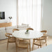 Angled lifestyle shot of Rigby Armchair – Natural with dining table in airy interior.