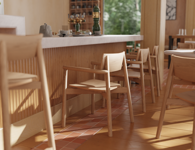 Close-up lifestyle shot of Andi Armchair Natural wooden chairs lined along a bar counter, highlighting smooth armrests, curved backrests, warm timber finish, and soft natural lighting in a café setting.