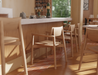 Close-up lifestyle shot of Andi Armchair Natural wooden chairs lined along a bar counter, highlighting smooth armrests, curved backrests, warm timber finish, and soft natural lighting in a café setting.