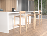 Modern kitchen island setting with multiple Andi Bar Stool - Natural - 75 cm Seat Height stools, featuring a white countertop, wood flooring, and large windows with outdoor view.
