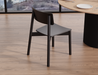 Rear angled view of Andi Dining Chair Black in a modern dining space with light wood flooring and round table, showcasing minimalist design and matte black finish.