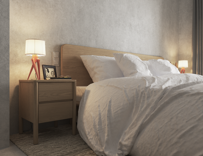 Natural wood bedside table with 2 drawers next to a natural wooden bed.  The table has a lamp and picture frame displayed on it.