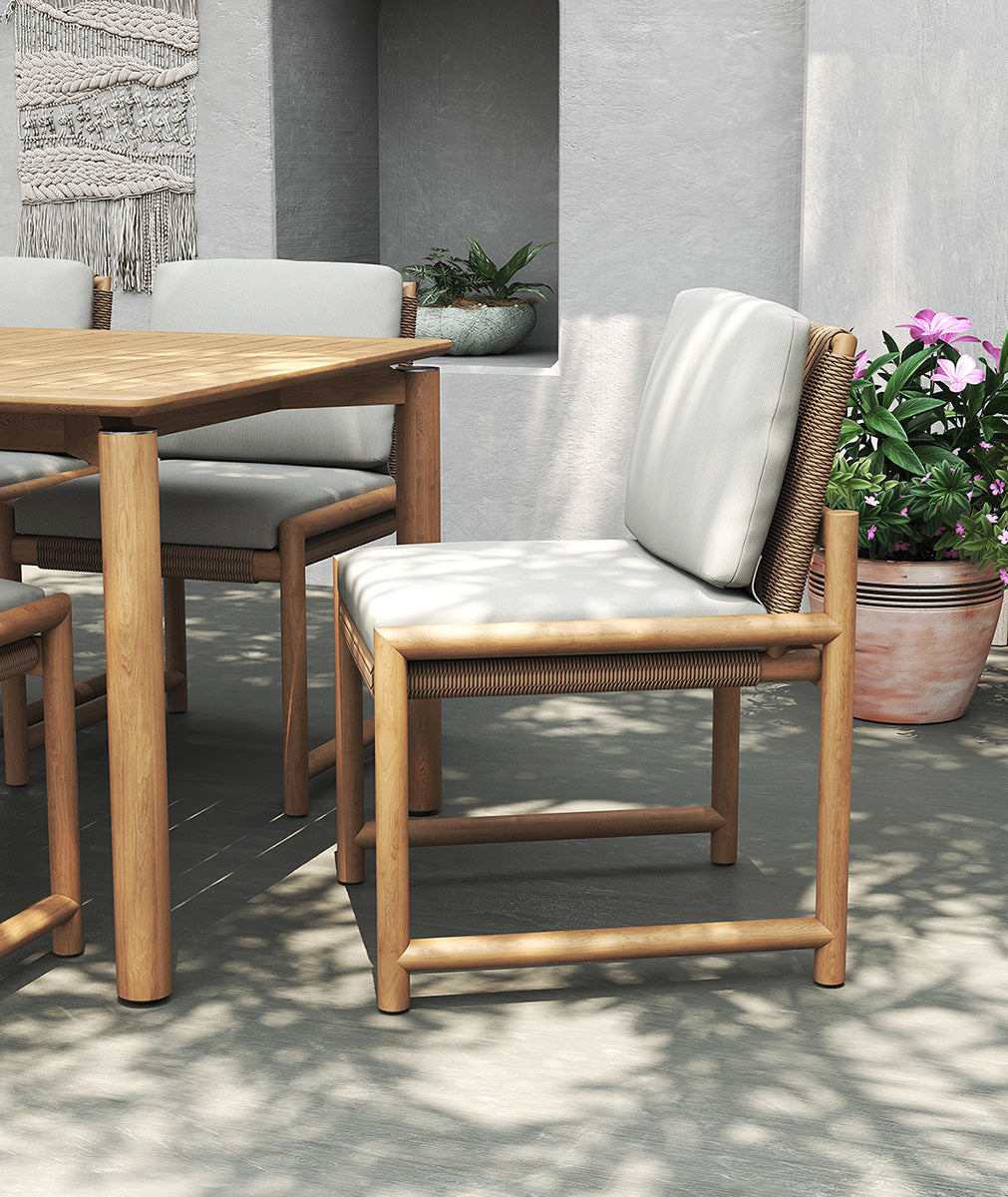 Esperance Outdoor Dining Chair in styled patio scene with teak dining table, textured grey wall, and potted plants.