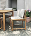 Esperance Outdoor Dining Chair in styled patio scene with teak dining table, textured grey wall, and potted plants.