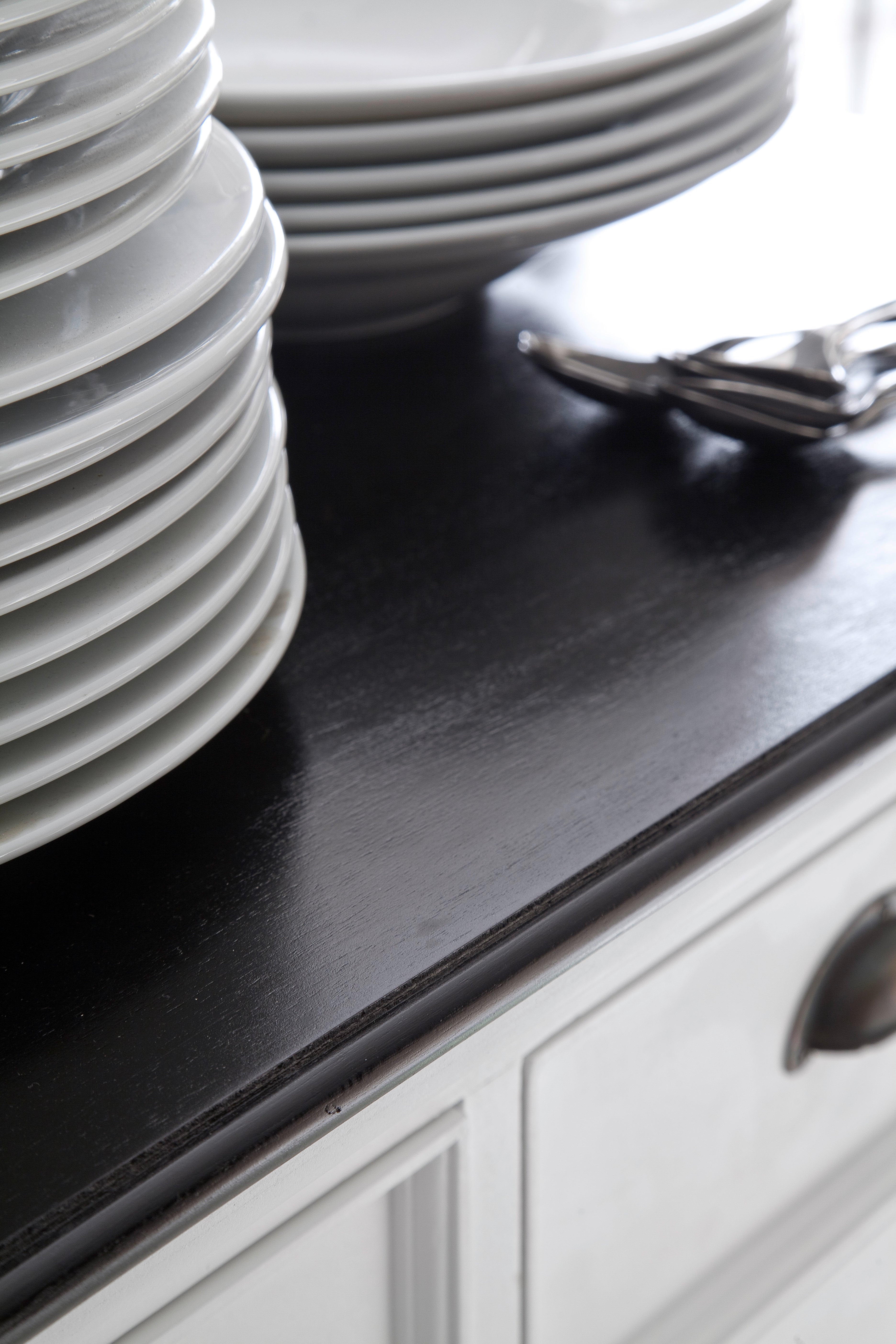 Close-up of the black timber top on the Halifax Contrast Buffet with 2 Baskets, styled with stacked plates and cutlery.