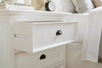 Close-up of an open drawer on the Halifax Grand Bedside Drawer Unit beside a bed, showing the black cup handle and white drawer front.