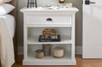 Halifax Grand Bedside Table styled beside a bed with books, lamp, decorative boxes and open shelves.