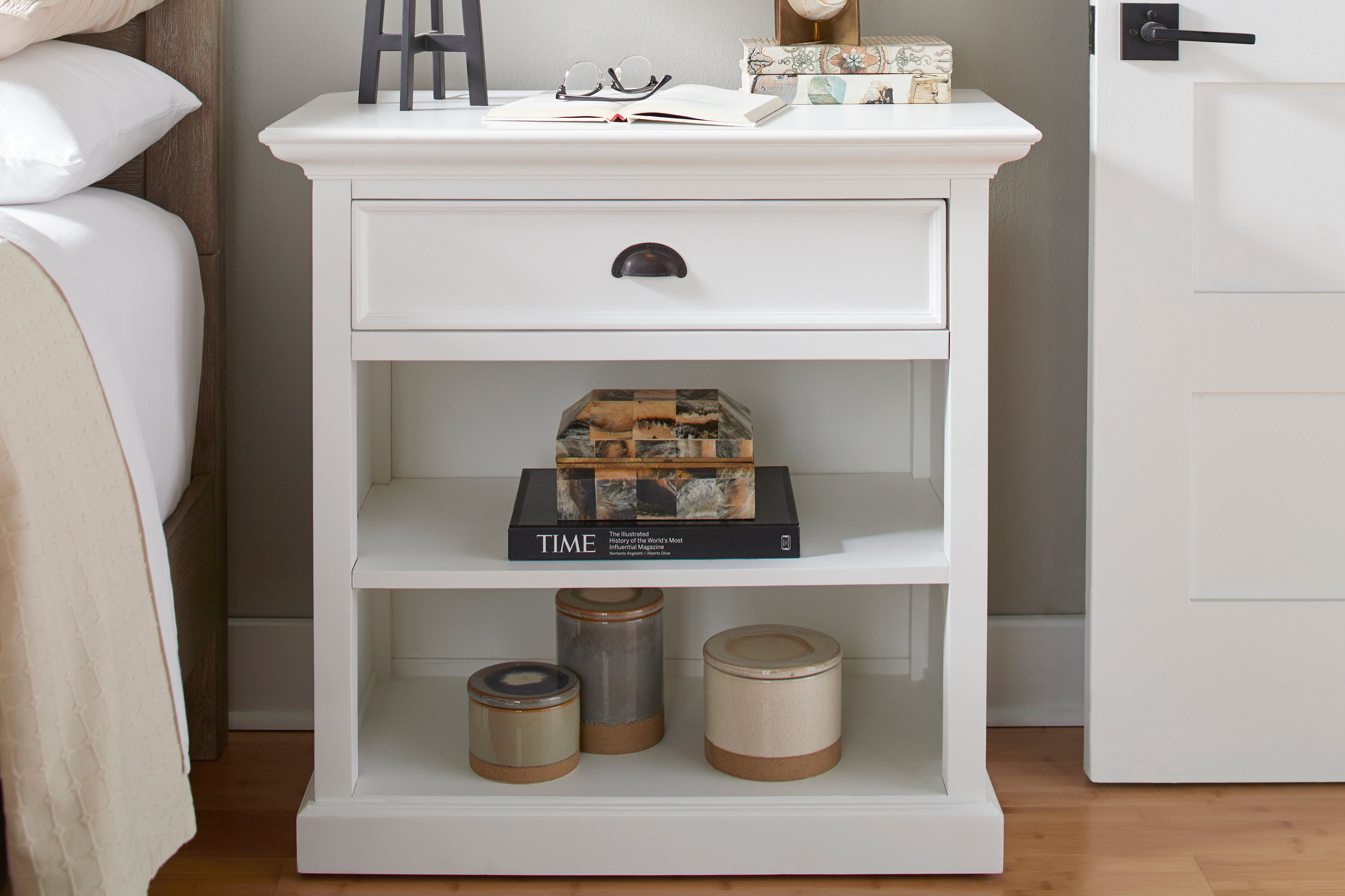 Halifax Grand Bedside Table styled beside a bed with books, lamp, decorative boxes and open shelves.