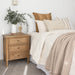 Lifestyle side view of Hamilton 3 drawer bedside table – Natural styled with vase and greenery beside bed.