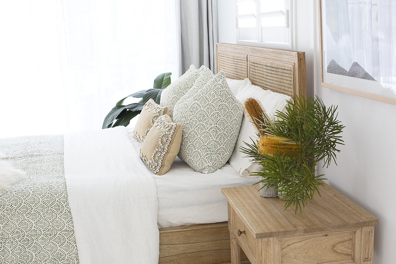 Hamilton Cane Bed Weathered Oak double bed close-up styling with textured neutral bedding, patterned cushions, soft throw blanket, and indoor greenery, highlighting natural oak frame and woven cane headboard detail.