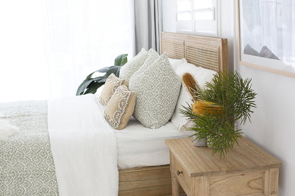 Hamilton Cane Bed Weathered Oak double bed close-up styling with textured neutral bedding, patterned cushions, soft throw blanket, and indoor greenery, highlighting natural oak frame and woven cane headboard detail.
