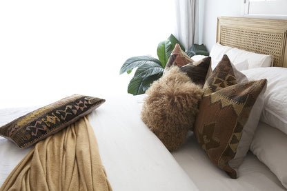 Hamilton Cane Bed Weathered Oak double bed close-up styling with textured neutral bedding, patterned cushions, soft throw blanket, and indoor greenery, highlighting natural oak frame and woven cane headboard detail.