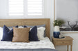Close view of Hamilton Cane Bed rattan headboard in Weathered Oak with layered cushions, white bedding and matching timber bedside
