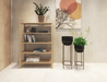 Wooden bookshelf with 4 shelves in a natural American oak finish next to 2 pots in stands with a painting on the wall behind them.