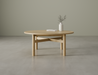 Nordica round wooden coffee table in natural oak finish with a white vase on a polished concrete floor.