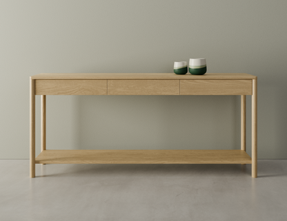 Front view of Nordica wooden console table in natural oak finish with 3 drawers on a polished concrete floor displaying 2 ceramic ornaments.