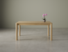 Front view of a small Nordica wooden dining table in natural oak finish with a flower in a vase on a polished concrete floor.