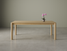 Front view of a medium Nordica wooden dining table in natural oak finish with a flower in a vase on a polished concrete floor.