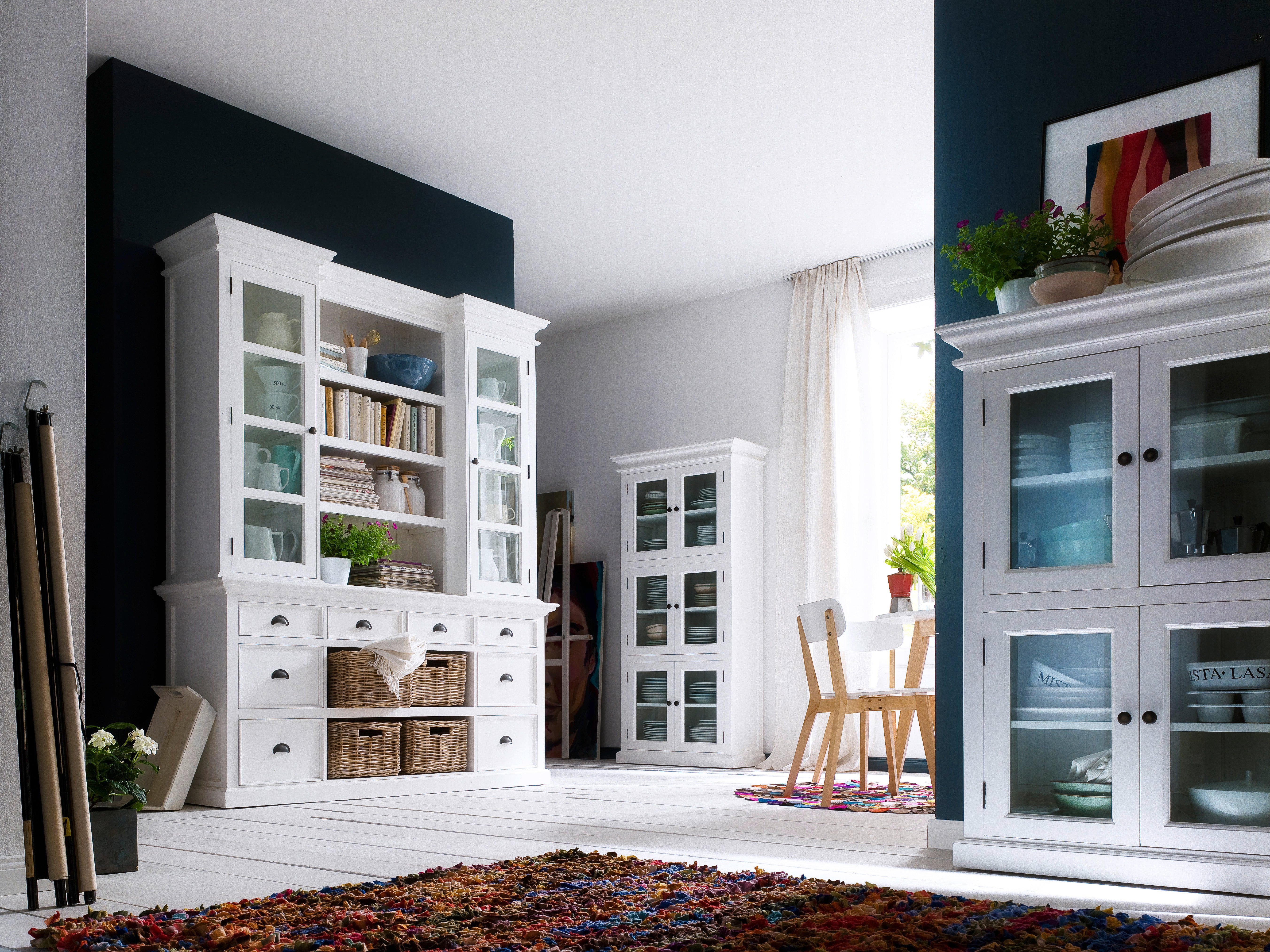 Traditional white timber cabinet with 6 glass doors in a room with white floor boards, large rug and other various hamptons style furniture.