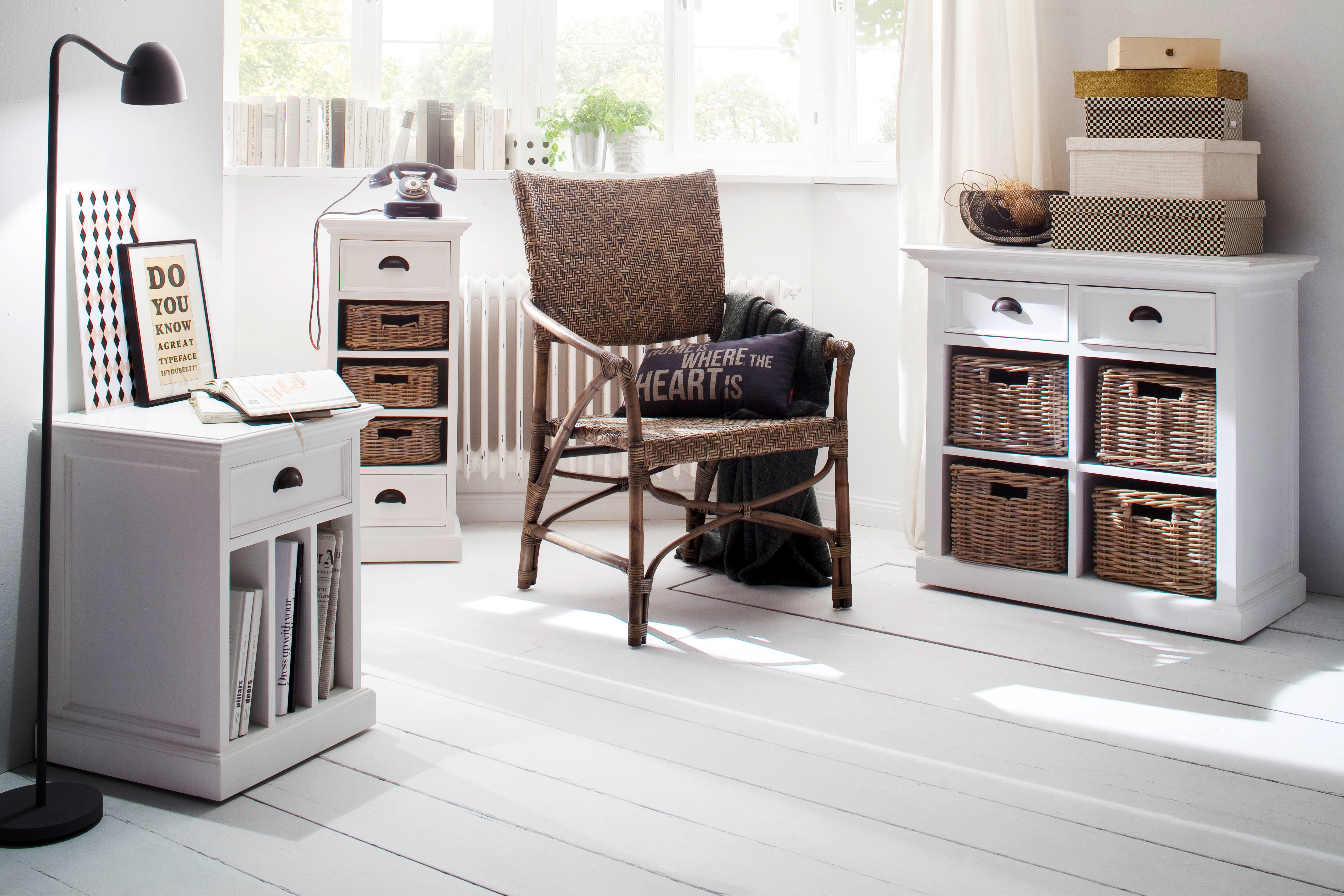 A bright coastal sitting area displaying a white timber bedside table with dividers, natural chair and two white wooden side tables with baskets.