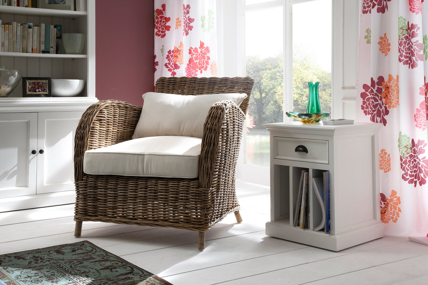 Casual setting of a white timber bedside table with dividers filled with books next to a wicker armchair and white timber buffet.
