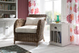Casual setting of a white timber bedside table with dividers filled with books next to a wicker armchair and white timber buffet.
