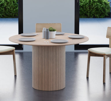 4 to 5 seater round dining table in natural American ash finish with 3 wooden chairs on a polished concrete floor.