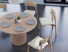 Slight aerial view of 4 to 5 seater round dining table in natural American ash finish with 4 wooden chairs on a polished concrete floor.