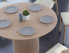 Close up aerial view of 4 to 5 seater round dining table in natural American ash finish displaying plates and cutlery with 4 wooden chairs on a polished concrete floor.