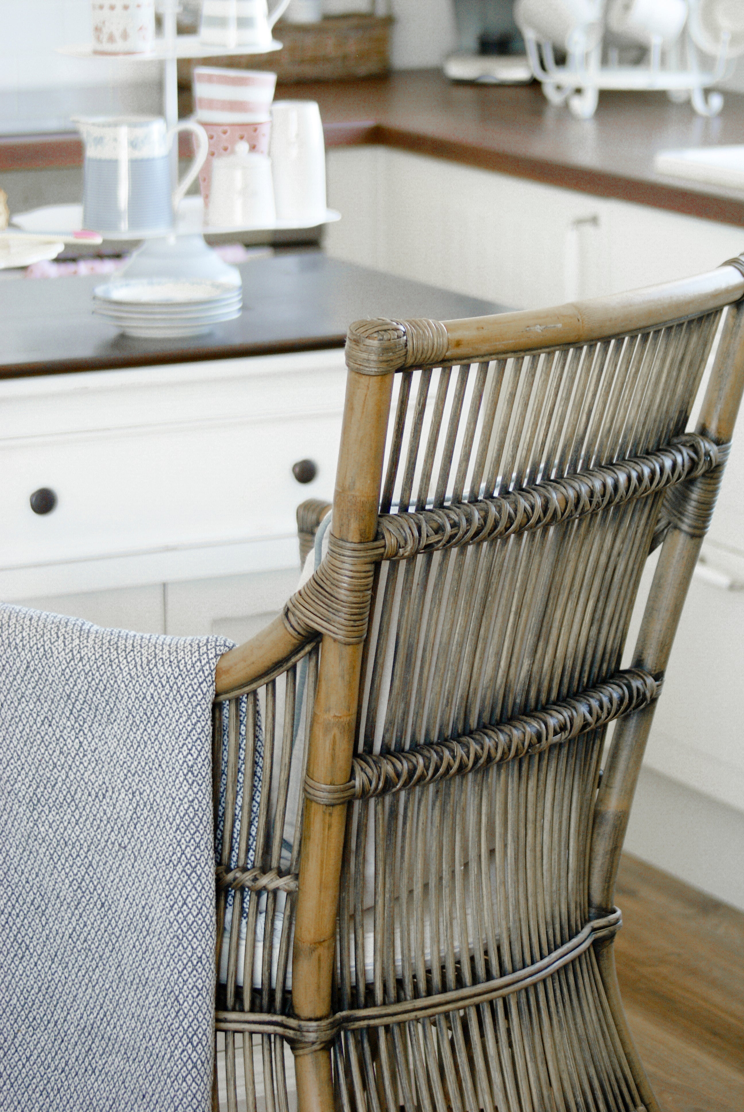 Close-up of a rattan dining chair with woven back detail and white seat cushion, styled beside a white kitchen island.