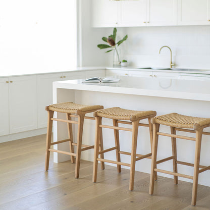 Three Zen Backless Bar Stools – Sand – Open Weave styled under a white waterfall-edge island bench in a light-filled modern kitchen.