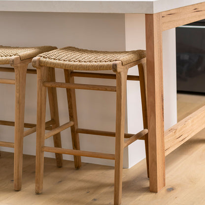 Close-up of Zen Backless Bar Stools – Sand – Open Weave tucked under a kitchen island with light timber flooring.