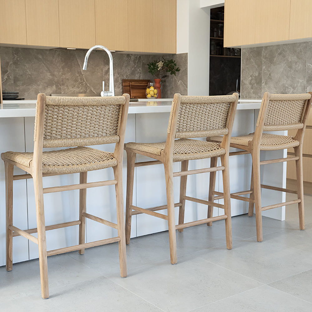 Close-up angled view of Zen Counter Stools – Sand – Close Weave at a kitchen island, showcasing detailed weave and sculpted teak frames.