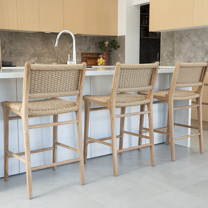 Close-up angled view of Zen Counter Stools – Sand – Close Weave at a kitchen island, showcasing detailed weave and sculpted teak frames.