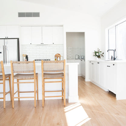 Interior kitchen setting featuring three Zen Bar Stools – Washed Grey – Open Weave styled at a white breakfast bar with timber floors.