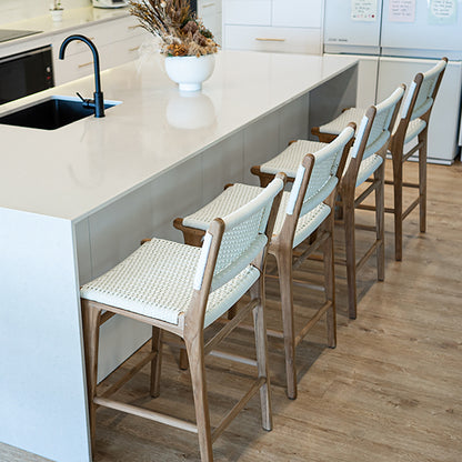 Interior kitchen scene with a row of Zen Counter Stools – White – Close Weave positioned along a white island bench on timber flooring.