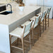 Interior kitchen scene with a row of Zen Counter Stools – White – Close Weave positioned along a white island bench on timber flooring.