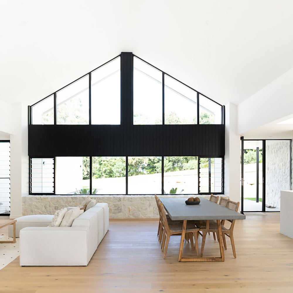 Wide view of a modern living and dining area featuring the Zen Dining Chair – Washed Grey – Open Weave and large windows.