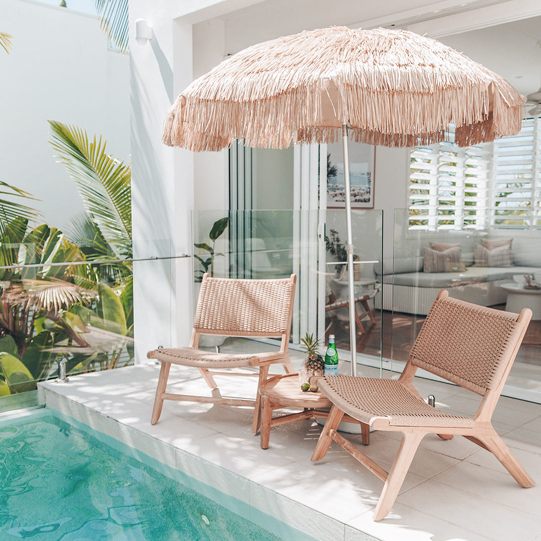 Relaxed poolside scene with Zen Lazy Chairs in Sand, tropical greenery, and natural umbrella for shaded outdoor lounging.