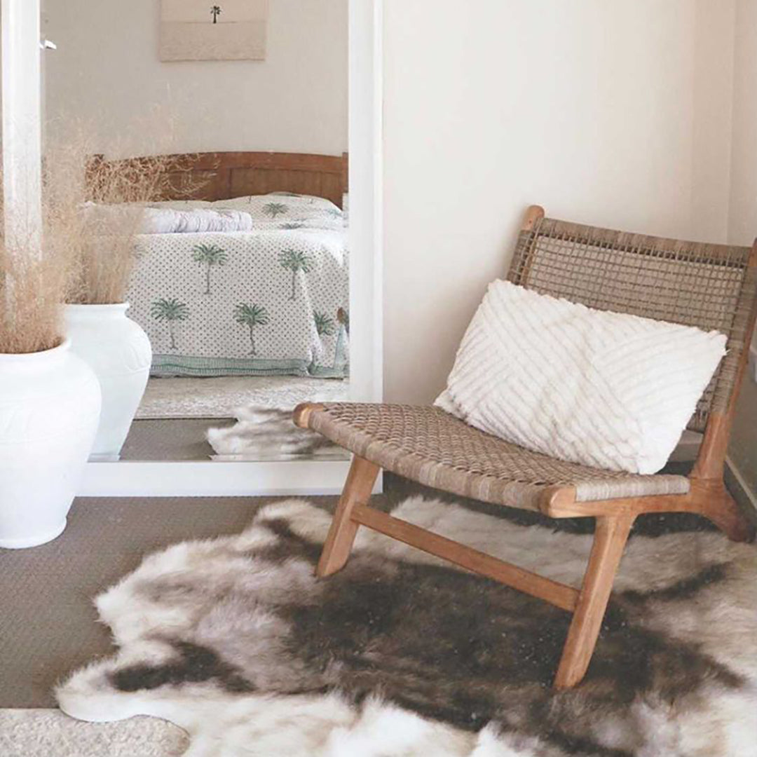 The Zen Lazy Chair – Washed Grey – Close Weave styled in a cozy corner with a textured white cushion and natural hide rug. Reflected in a mirror, the chair’s soft neutral tones and organic textures bring warmth to relaxed interiors.