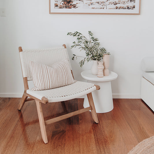 Single Zen Lazy Chair - White - Open Weave placed beside a modern white side table with sculptural vases and a leafy branch. The chair features a handwoven open-grid seat in crisp white with a natural teak wood frame, styled with a striped lumbar cushion for added comfort and visual interest.
